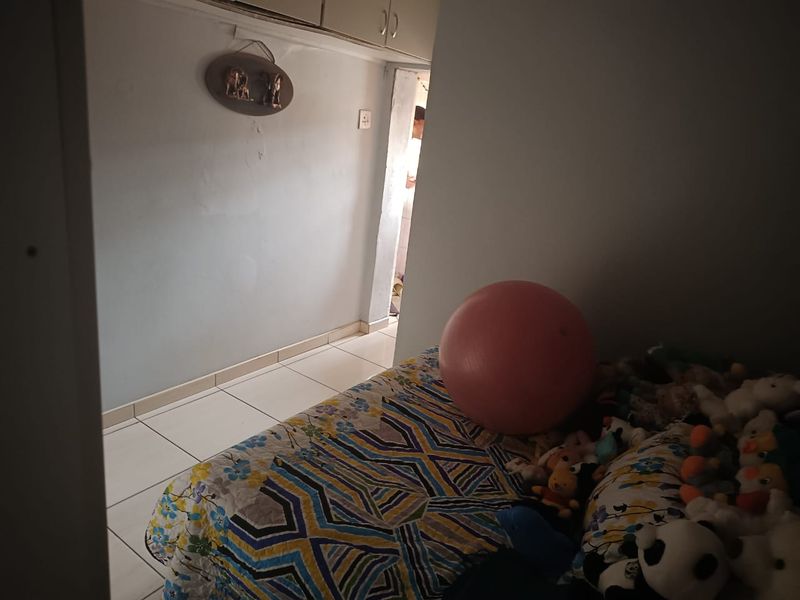 A bedroom featuring tiled flooring and built-in cupboards, currently showing signs of wear on the wall surfaces.