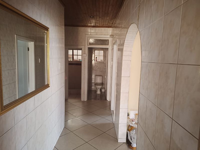 A tiled hallway featuring a timber ceiling and an arched entryway leading to a bathroom area.