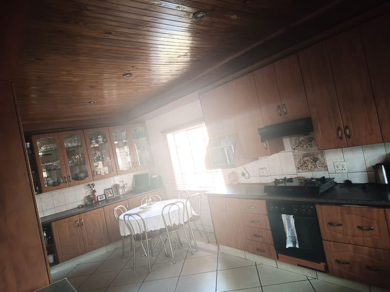A spacious kitchen featuring wooden cabinetry, a built-in oven with gas hob, tiled flooring, and a distinctive wooden ceiling.