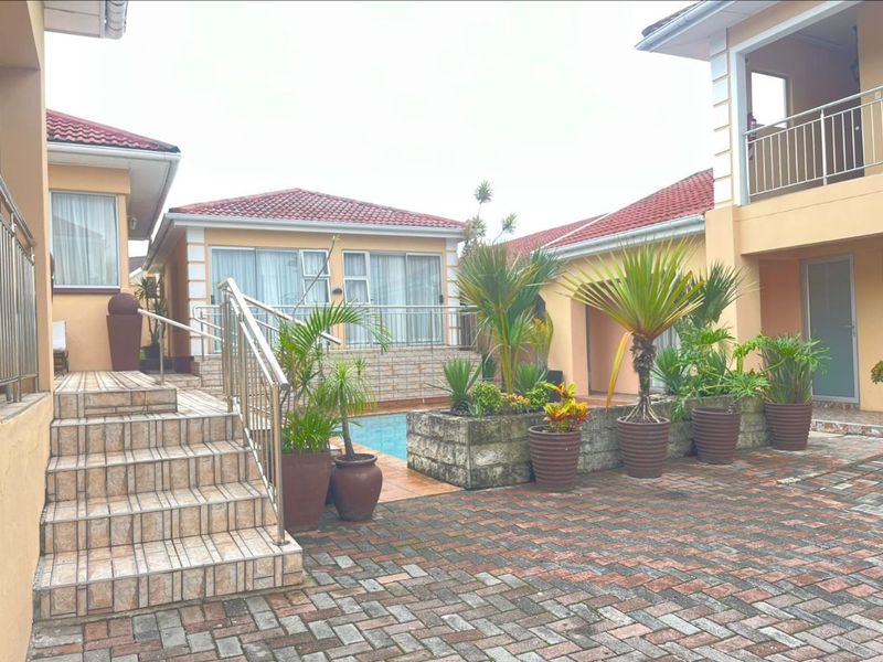 Outdoor courtyard area featuring a swimming pool, tiled staircase with stainless steel railings, and brick paving, connecting multiple sections of the property.