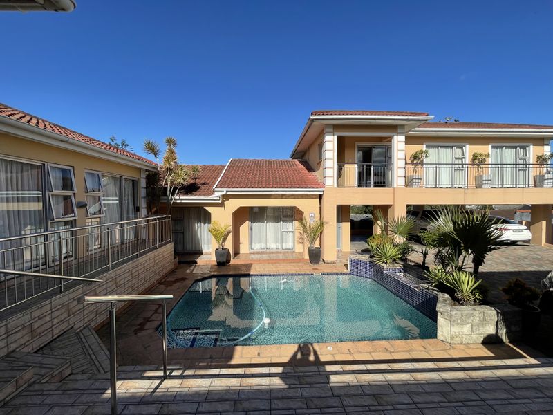 A well-maintained outdoor pool area featuring a tiled patio, surrounding paved surfaces, and a balcony overlooking the swimming pool.