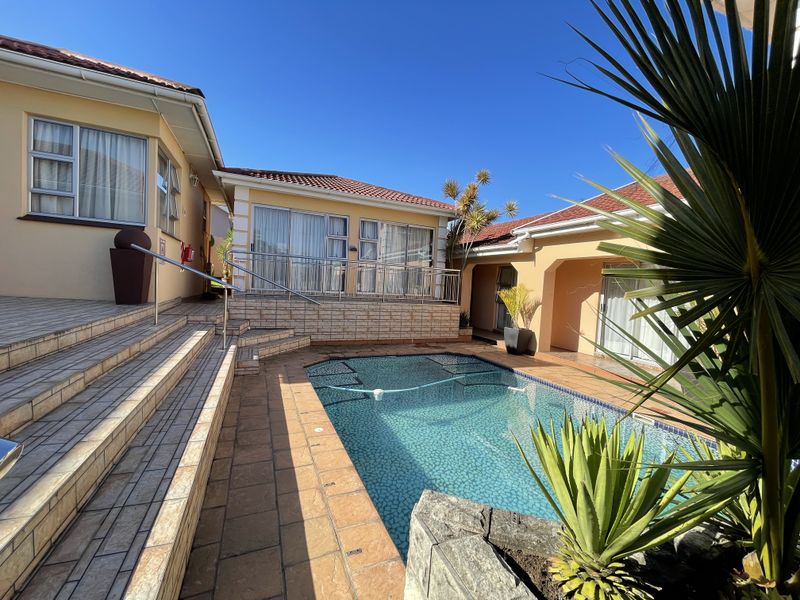 A well-maintained outdoor pool area featuring a tiled patio, tiered steps with metal handrails, and direct access to the surrounding building wings.