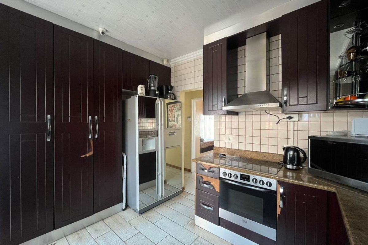 Kitchen featuring dark wood cabinetry, stone countertops, tiled backsplash, and built-in oven with extractor fan. Shows signs of wear on cabinet finishes.