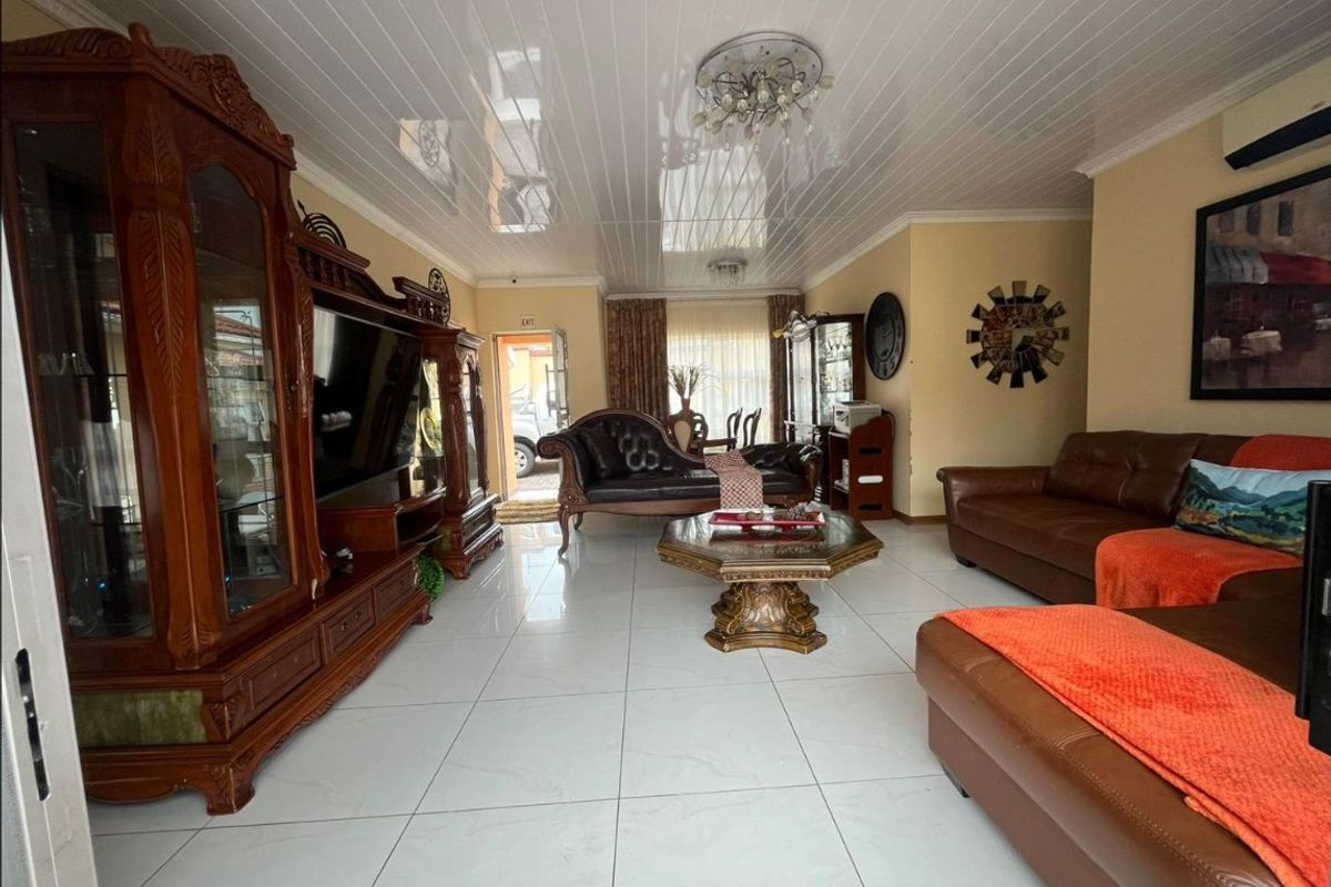 Spacious living room featuring glossy white ceiling panels, large format porcelain floor tiles, and a wall-mounted air conditioning unit.