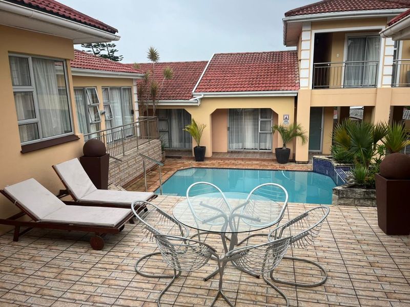 A well-maintained outdoor pool area featuring a tiled patio, stone accents, and direct access to the surrounding residential building wings.