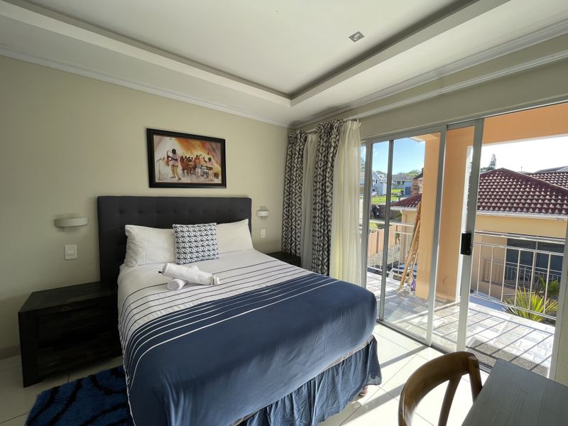 A well-maintained bedroom featuring a tray ceiling, recessed lighting, and large sliding glass doors that open onto a private balcony.