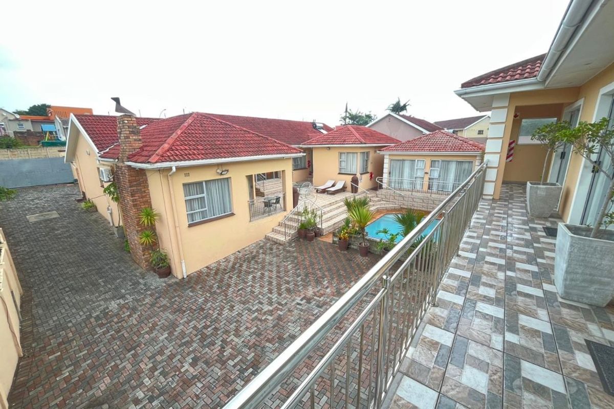 Rear view of the property featuring a paved courtyard, swimming pool, and a spacious tiled balcony with stainless steel balustrades.