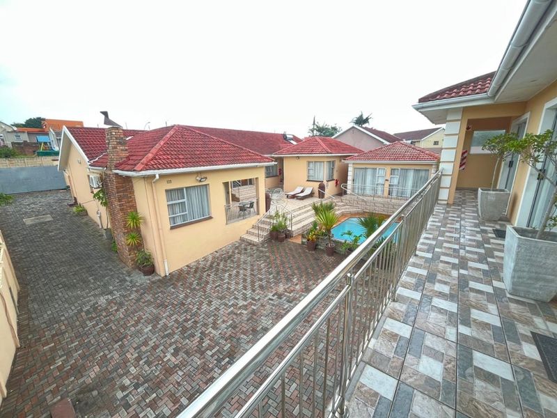 Rear view of the property featuring a paved courtyard, swimming pool, and a spacious tiled balcony with stainless steel balustrades.