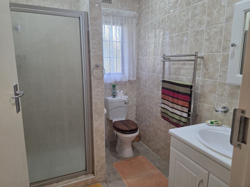 A functional bathroom featuring a shower enclosure, vanity unit with basin, toilet, and a heated towel rail, finished with neutral wall and floor tiling.