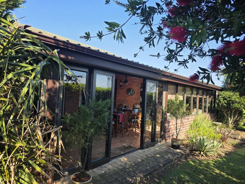 A covered patio area featuring brick walls, large glass sliding doors, and tiled flooring, providing a seamless transition to the garden.