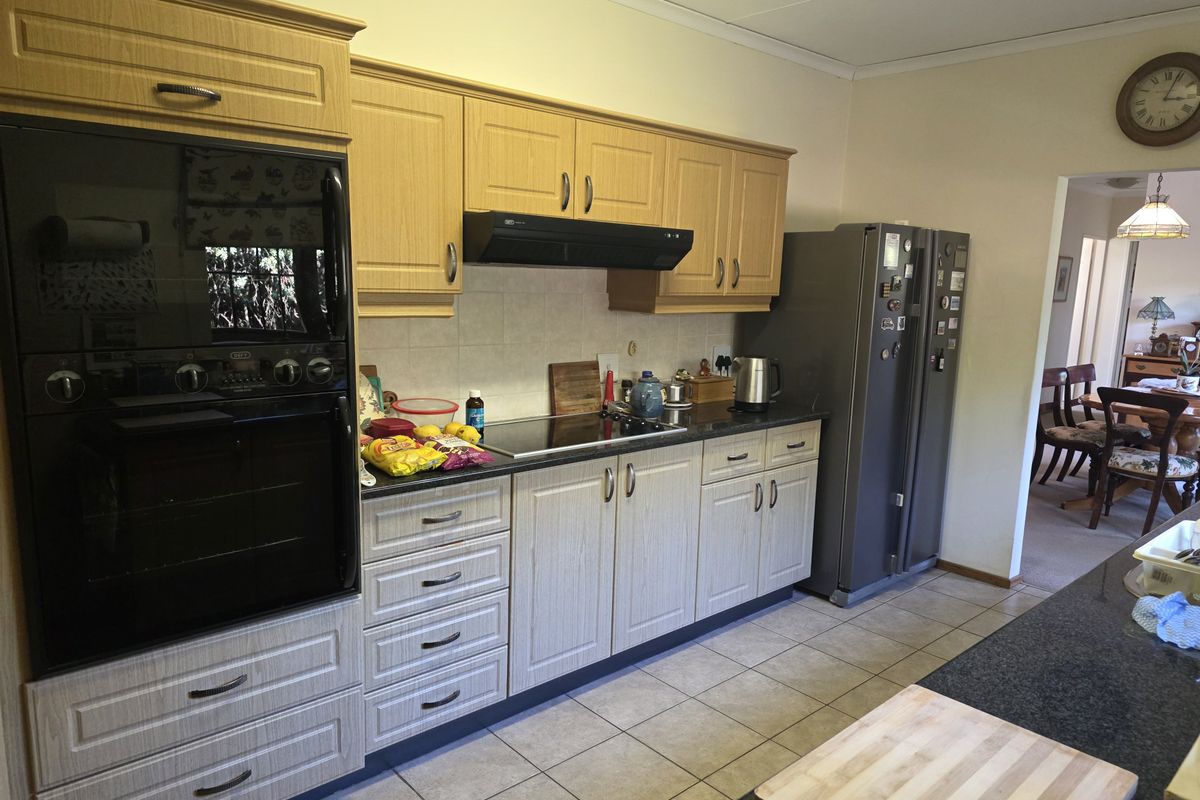 A functional kitchen featuring light wood-finish cabinetry, granite countertops, a built-in oven, and an electric hob, with tiled flooring throughout.