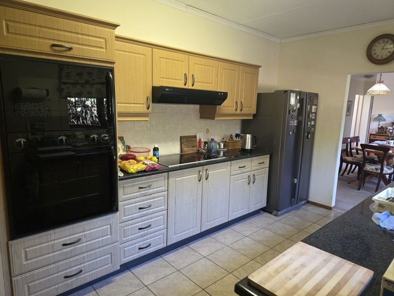 A functional kitchen featuring light wood-finish cabinetry, granite countertops, a built-in oven, and an electric hob, with tiled flooring throughout.