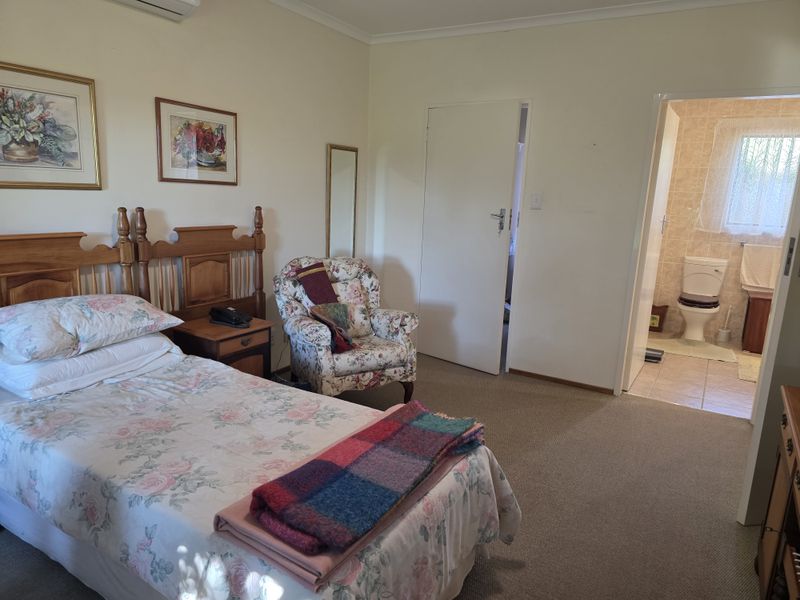 A carpeted bedroom featuring an en-suite bathroom with a toilet and tiled flooring, complemented by a wall-mounted air conditioning unit.
