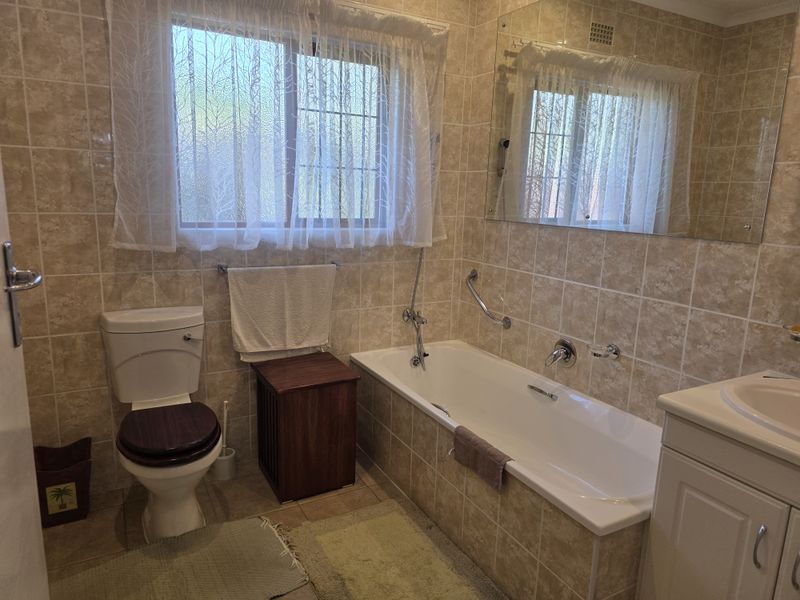 A functional bathroom featuring a built-in bathtub, vanity cabinet, toilet, and neutral wall tiling, offering a clean and practical layout.