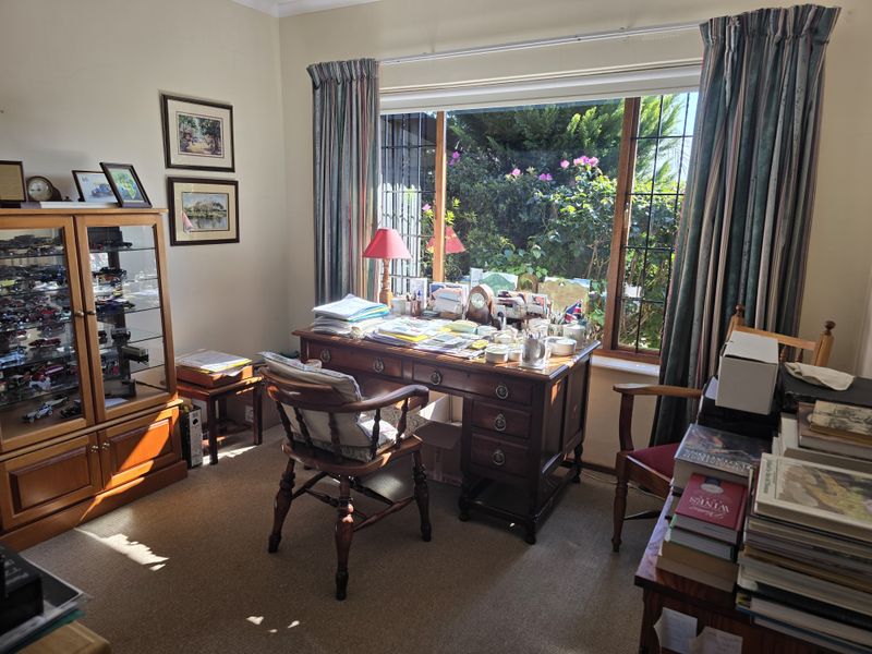 A home office space featuring a large window with garden views and carpeted flooring.