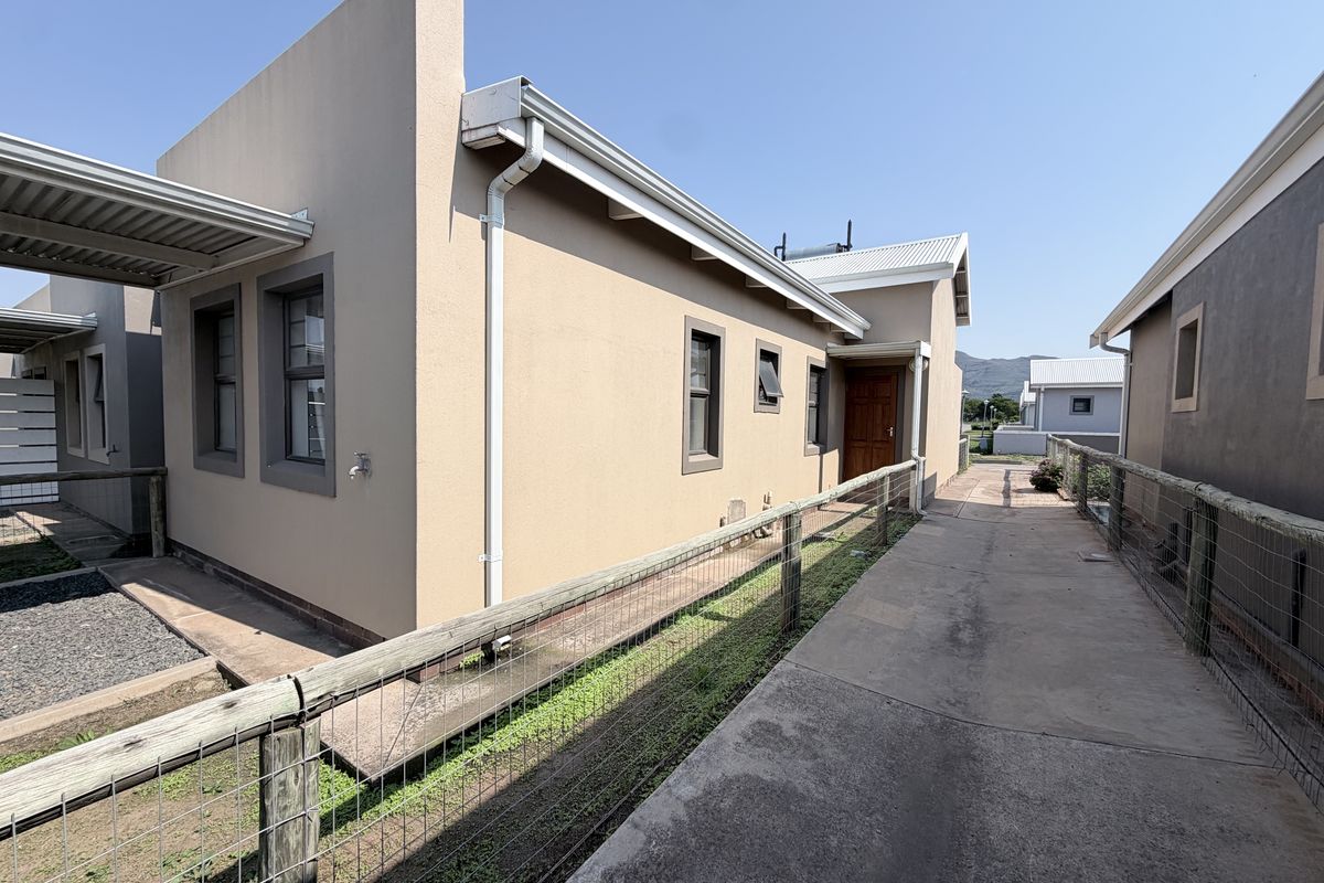 Rear exterior view of the townhouse featuring a concrete walkway, timber fencing, and functional guttering systems under a clear sky.