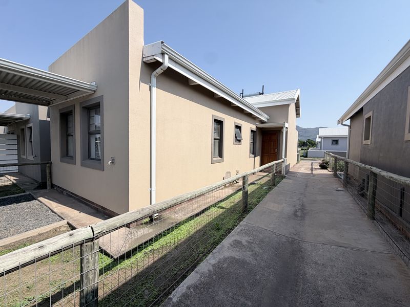 Rear exterior view of the townhouse featuring a concrete walkway, timber fencing, and functional guttering systems under a clear sky.