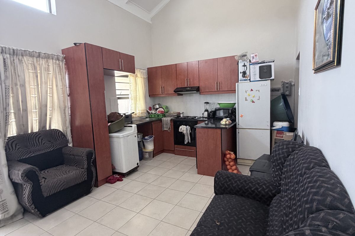 Open-plan kitchen and living area featuring high vaulted ceilings with exposed rafters, tiled flooring, and functional laminate cabinetry with granite countertops.