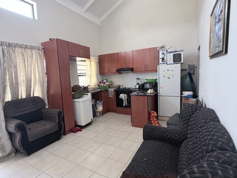 Open-plan kitchen and living area featuring high vaulted ceilings with exposed rafters, tiled flooring, and functional laminate cabinetry with granite countertops.
