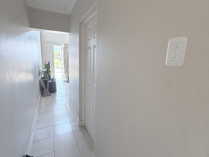 A neutral-toned hallway featuring tiled flooring and coving, providing a clean transition between living spaces.