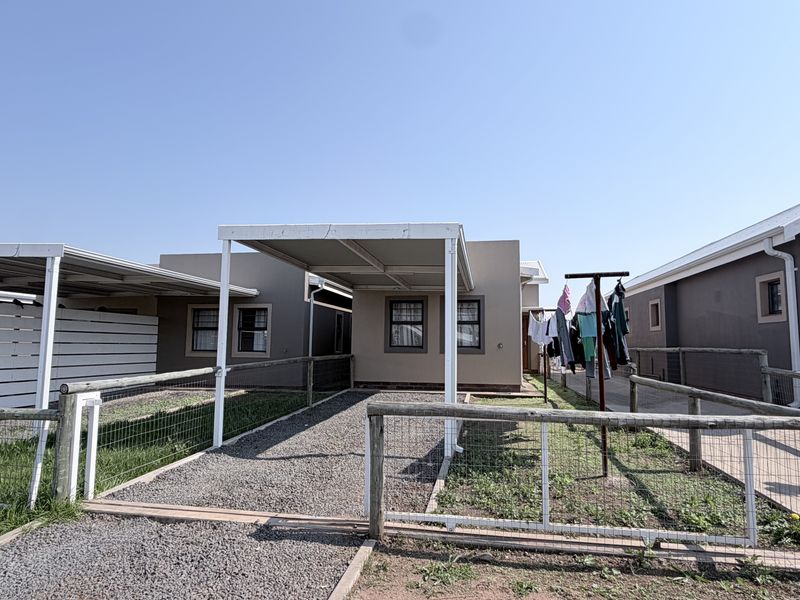 Front exterior view of a townhouse featuring a gravel driveway, covered carport, and wire mesh perimeter fencing.