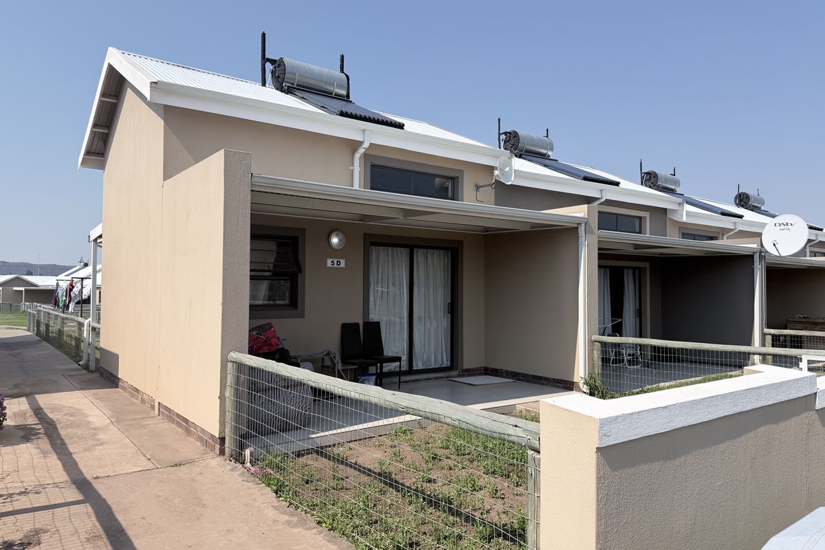 Front view of a townhouse unit featuring a covered patio, solar water heating system, and a small private garden area with wire fencing.