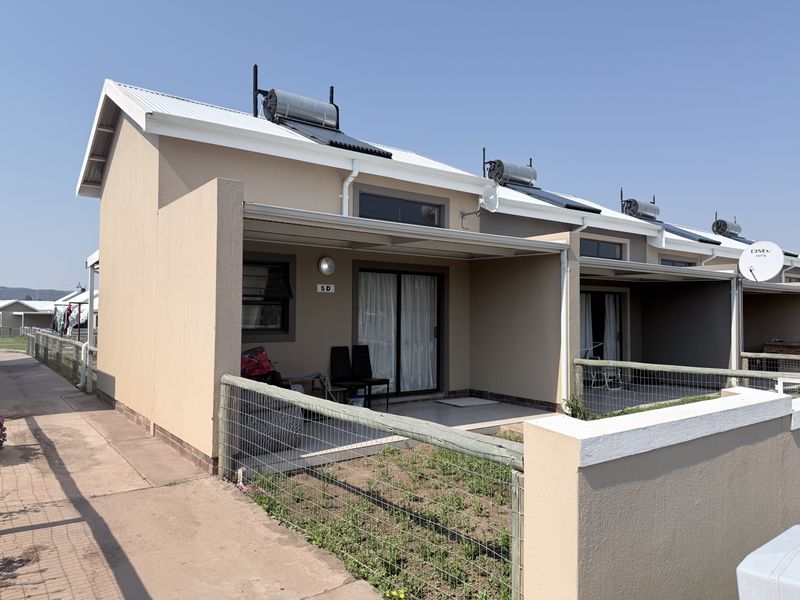 Front view of a townhouse unit featuring a covered patio, solar water heating system, and a small private garden area with wire fencing.