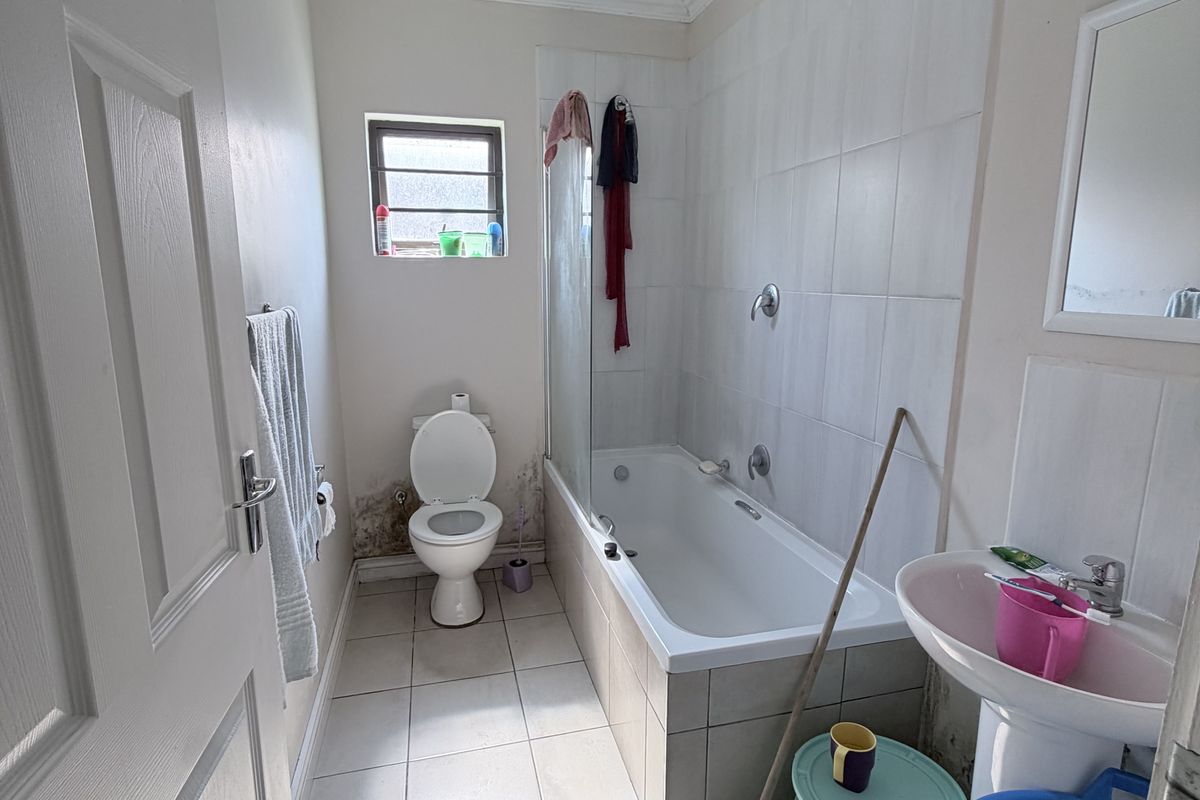 A functional bathroom featuring a bathtub with shower screen, pedestal basin, and toilet, requiring some maintenance to address visible wall damage.