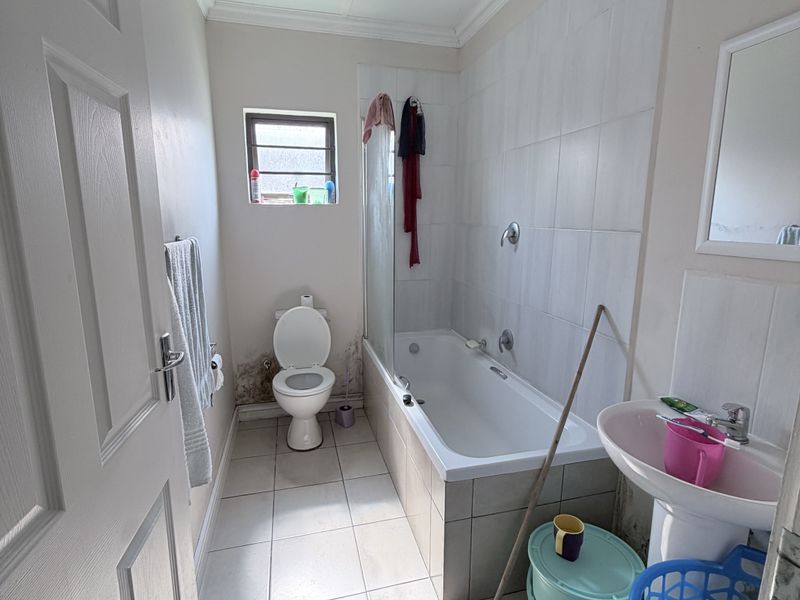 A functional bathroom featuring a bathtub with shower screen, pedestal basin, and toilet, requiring some maintenance to address visible wall damage.