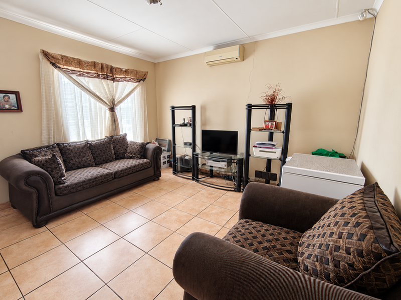 A living room featuring ceramic floor tiles, a wall-mounted air conditioning unit, and coved ceilings, providing a functional space for relaxation.