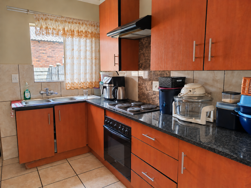 A functional kitchen featuring wood-finish cabinetry, dark granite-look countertops, a built-in oven with hob, and a double sink with tiled backsplash.