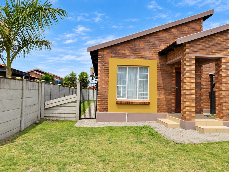 A well-maintained rear exterior view featuring a face brick facade, paved walkway, tiled entrance steps, and a secure precast concrete boundary wall.