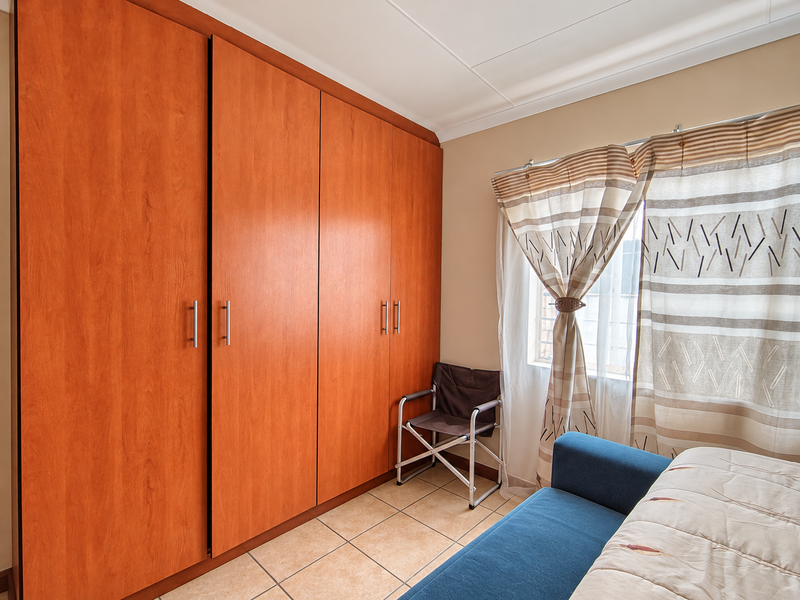 A bedroom featuring large built-in wooden cupboards, tiled flooring, and a window with curtains.