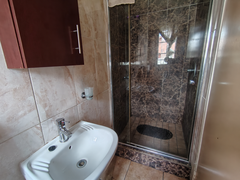 A compact bathroom featuring a glass-enclosed shower with dark marble-effect tiling, a white ceramic basin with chrome tap, and a wall-mounted storage cabinet.
