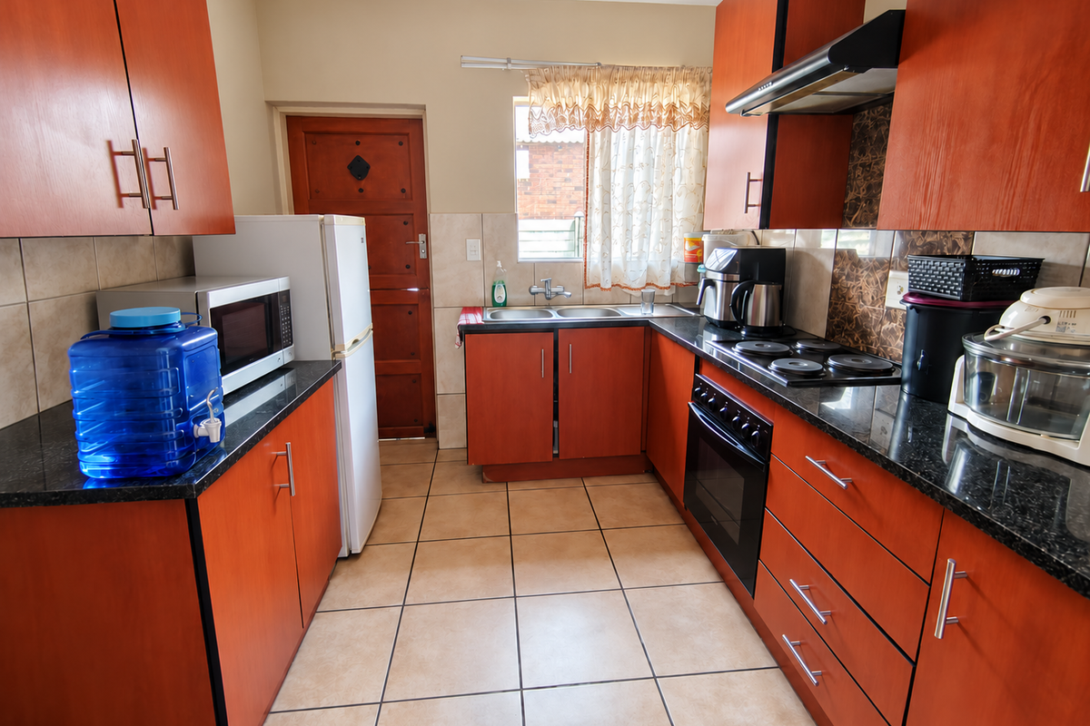 A functional kitchen featuring wood-finish cabinetry, granite countertops, a double basin sink, and built-in cooking appliances with tiled flooring throughout.