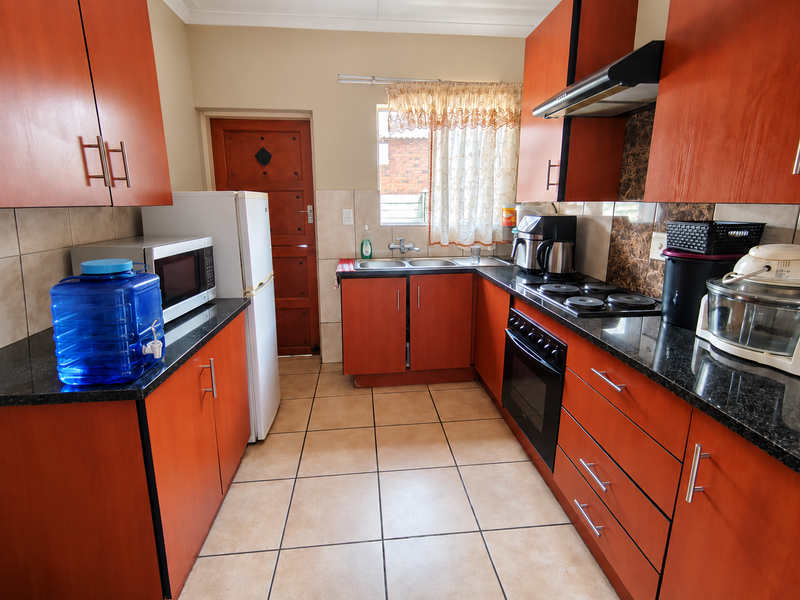 A functional kitchen featuring wood-finish cabinetry, granite countertops, a double basin sink, and built-in cooking appliances with tiled flooring throughout.