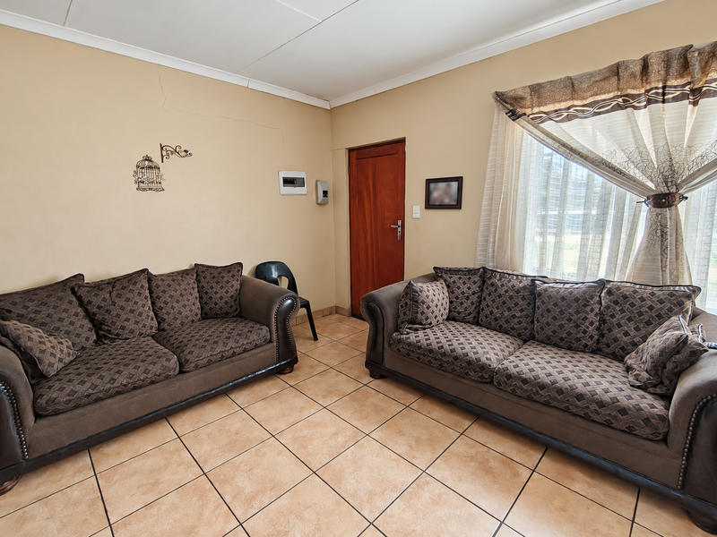 A living room featuring ceramic floor tiles, a timber door, and coved ceilings, showing signs of wear including visible wall cracks.