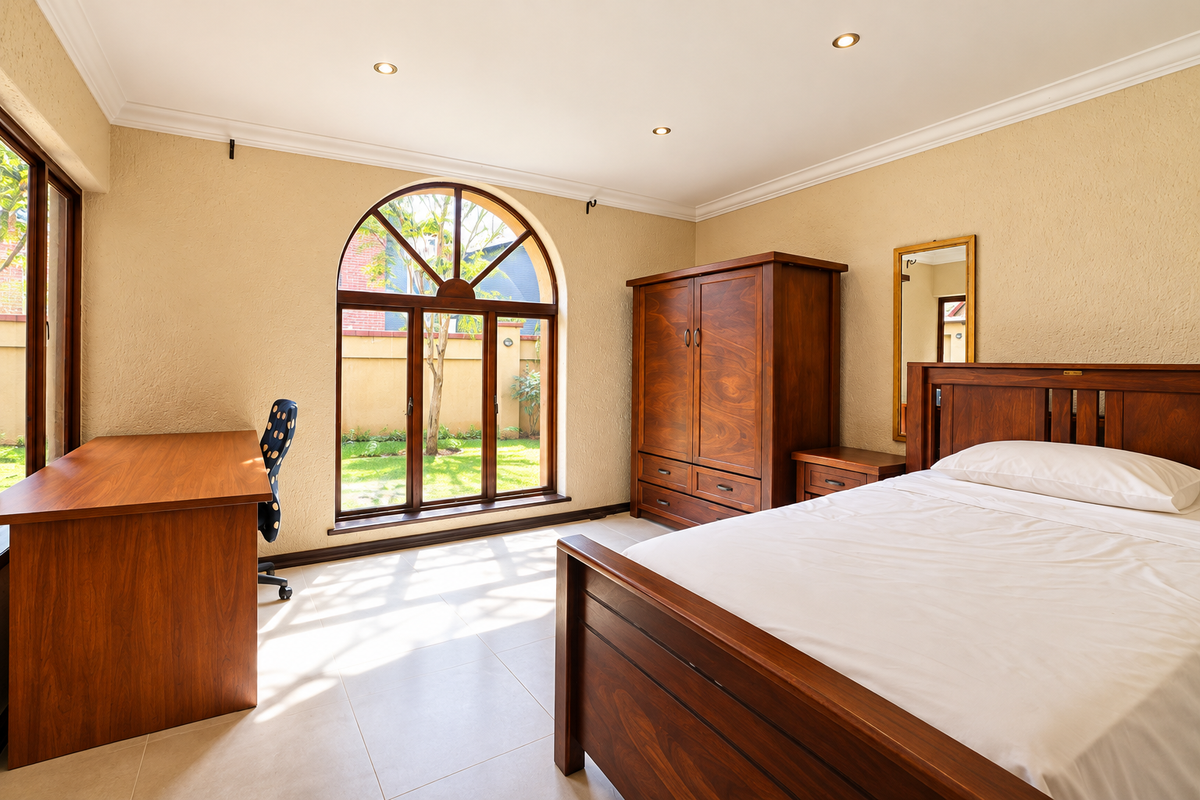 A well-maintained bedroom featuring tiled flooring, coved cornicing, recessed downlights, and a distinctive arched window overlooking the garden.