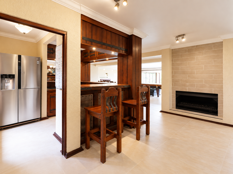 A well-maintained interior space featuring a built-in wooden bar, a modern tiled fireplace, and neutral floor tiling throughout.