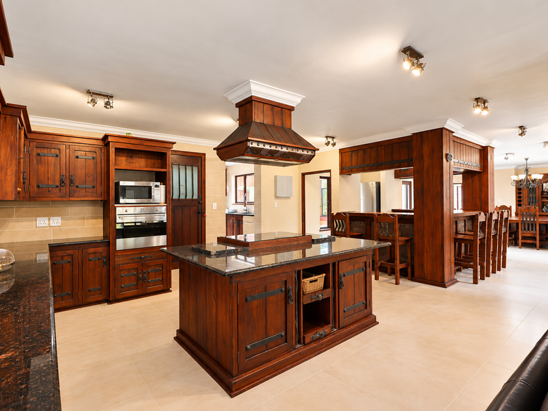 Spacious open-plan kitchen featuring custom timber cabinetry, granite countertops, a central island with breakfast bar, and integrated appliances in a warm, traditional style.