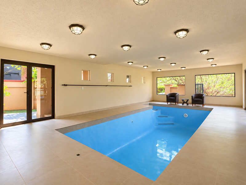 Spacious indoor pool area featuring tiled flooring, multiple recessed ceiling lights, and large windows providing natural light and garden views.