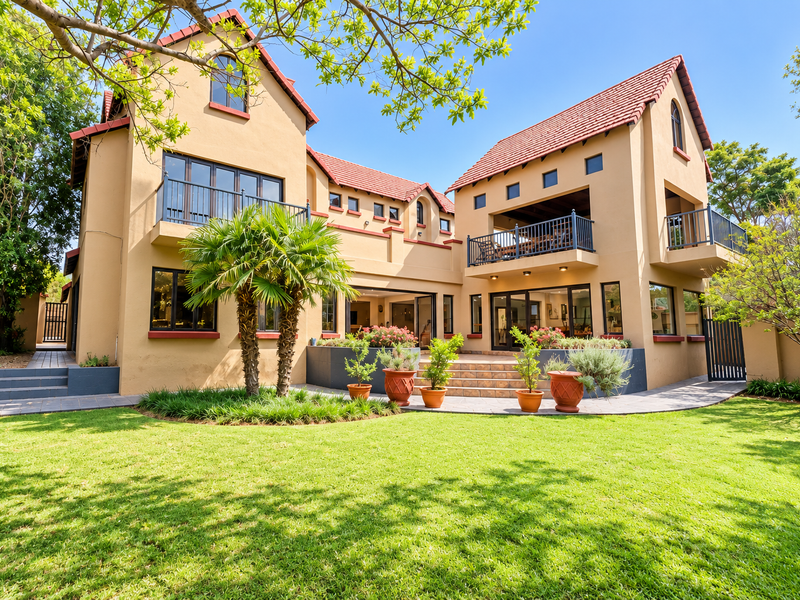 A well-maintained rear exterior view of a multi-story house featuring a landscaped garden, paved terrace, balconies, and large sliding glass doors.