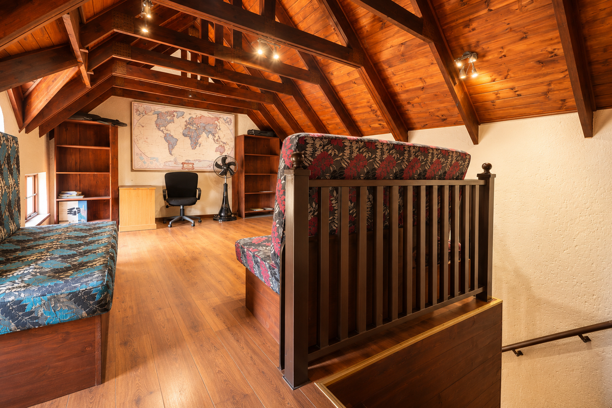 A cozy loft living area featuring exposed timber roof trusses, warm wood ceiling cladding, laminate flooring, and built-in timber shelving units.