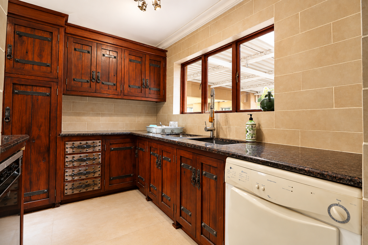 A rustic-style kitchen featuring dark wood cabinetry, granite countertops, a tiled backsplash, and a functional sink area with a gooseneck faucet.