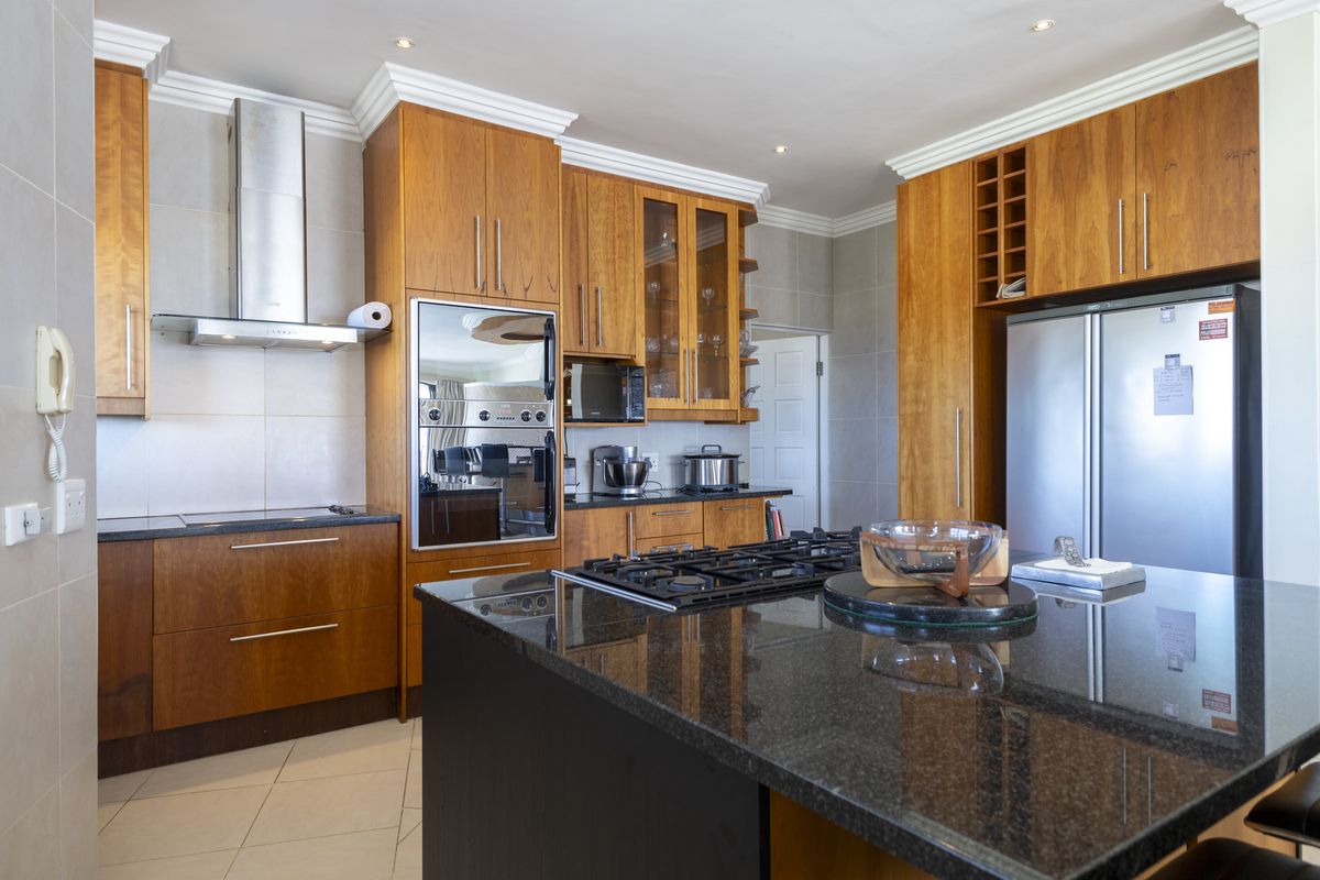 A well-appointed kitchen featuring warm wooden cabinetry, granite countertops, a central island with a gas hob, and integrated stainless steel appliances.