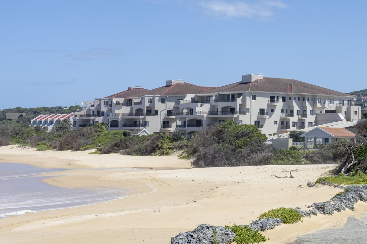 A view of the apartment complex exterior featuring multiple balconies and a tiled roof, situated directly along the sandy coastline.
