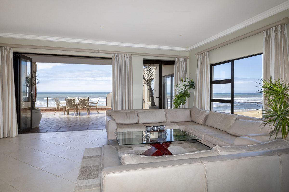Spacious living room featuring tiled floors, crown molding, and large sliding doors that open onto a balcony with expansive ocean views.