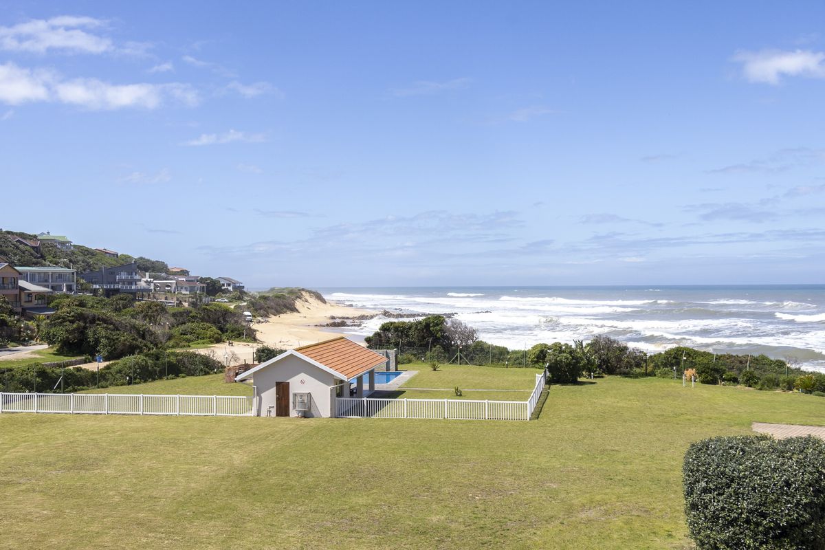 An elevated view of a coastal property featuring a spacious lawn, a pool house, and a swimming pool overlooking the ocean.
