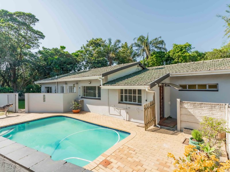 Outdoor pool area featuring a paved deck, swimming pool, and surrounding boundary walls, set against a backdrop of mature trees.