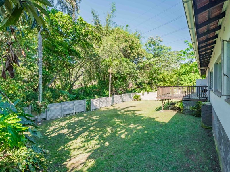 A spacious rear garden featuring a raised timber deck, established trees, and perimeter fencing, providing a private outdoor area.